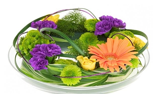 Centro floral en cuenco con claveles morados, gerbera naranja y rosas amarillas