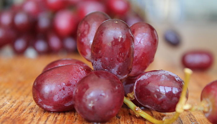 Granos de uva roja brillantes sobre una tabla de madera