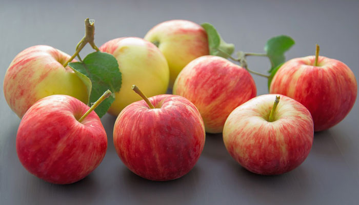 Manzanas rojas y amarillas con hojas, sobre una mesa gris